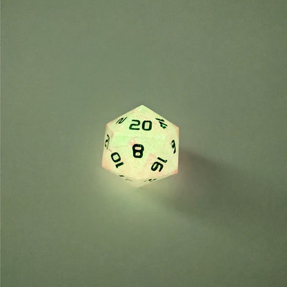 A high angle photo of a standard d20 glowing slightly green with pink/purple swirls and green numbers with the 20 face up on a white background.