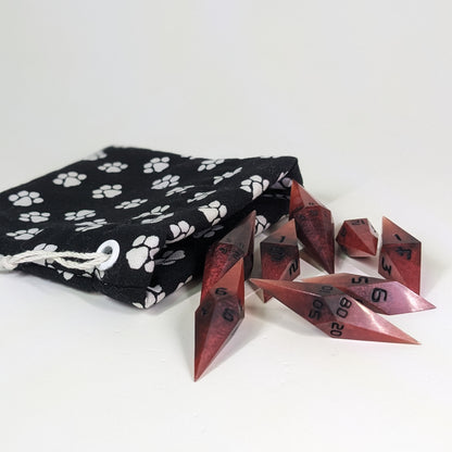 Mixed shades of red with black numbering diamond handmade dice spilling out of a (color description) drawstring bag on a white background. The set features 2 d20s and matching resin dice, showcasing the unique shape of these artisan dice.