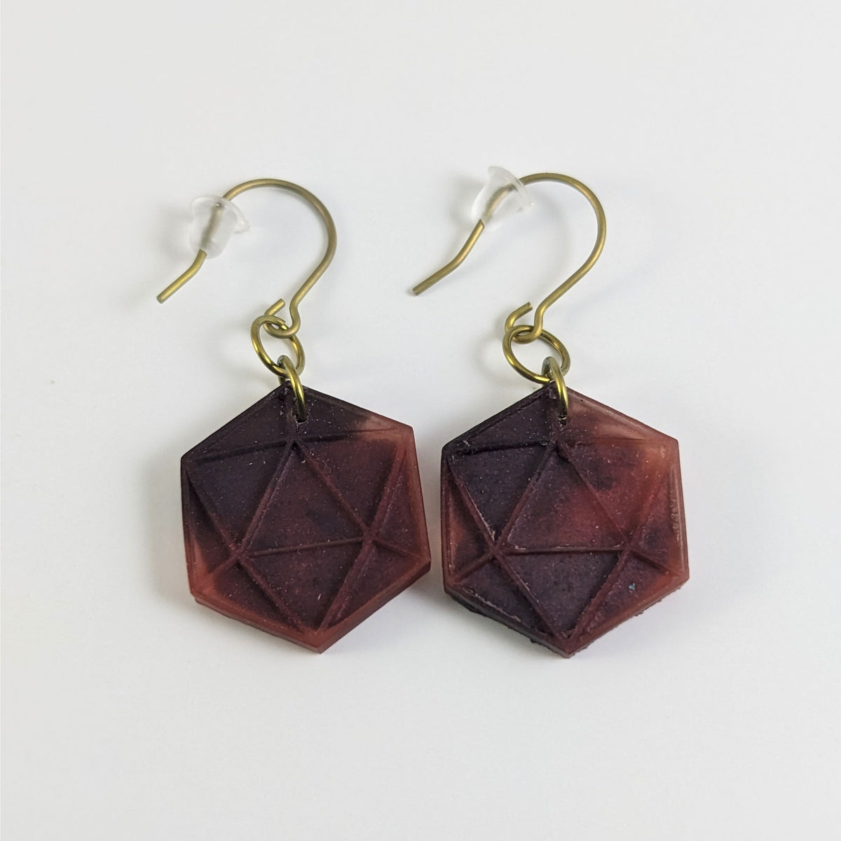 A pair of maroon and red dangly, flat d20 earrings with gold color titanium and niobium hardware and bell shaped rubber backs on a white background.