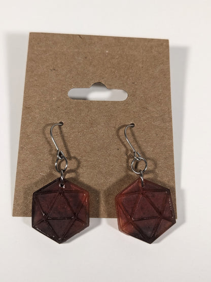 A pair of maroon and red dangly, flat d20 earrings with silver color titanium and niobium hardware on a kraft earring card on a white background.