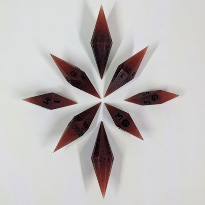 A complete set of diamond shaped resin dice featuring 2 d20s. These handmade dice are mixed shades of red with black numbers and are clustered in a circle with the bottom points angled toward a central point on a white background.