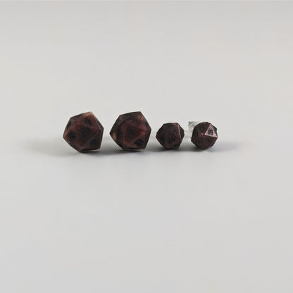 Two pairs of handmade d20 earrings with titanium hardware that are swirls of red with black numbers on a white background sit in a line with the larger pair on the left and the smaller pair on the right. The earrings on the left of each pair centers the 20 face and the earrings on the right of each pair centers the 1 face.