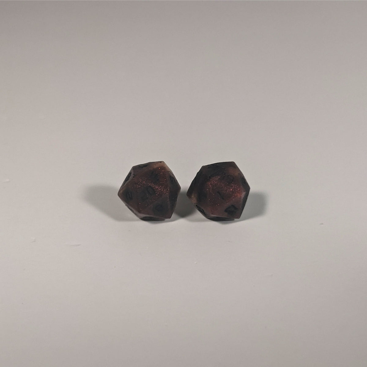 A single pair of the larger size handmade d20 earrings with titanium hardware that are swirls of red with black numbers on a white background. The earring on the left centers the 20 face and the earring on the right centers the 1 face.