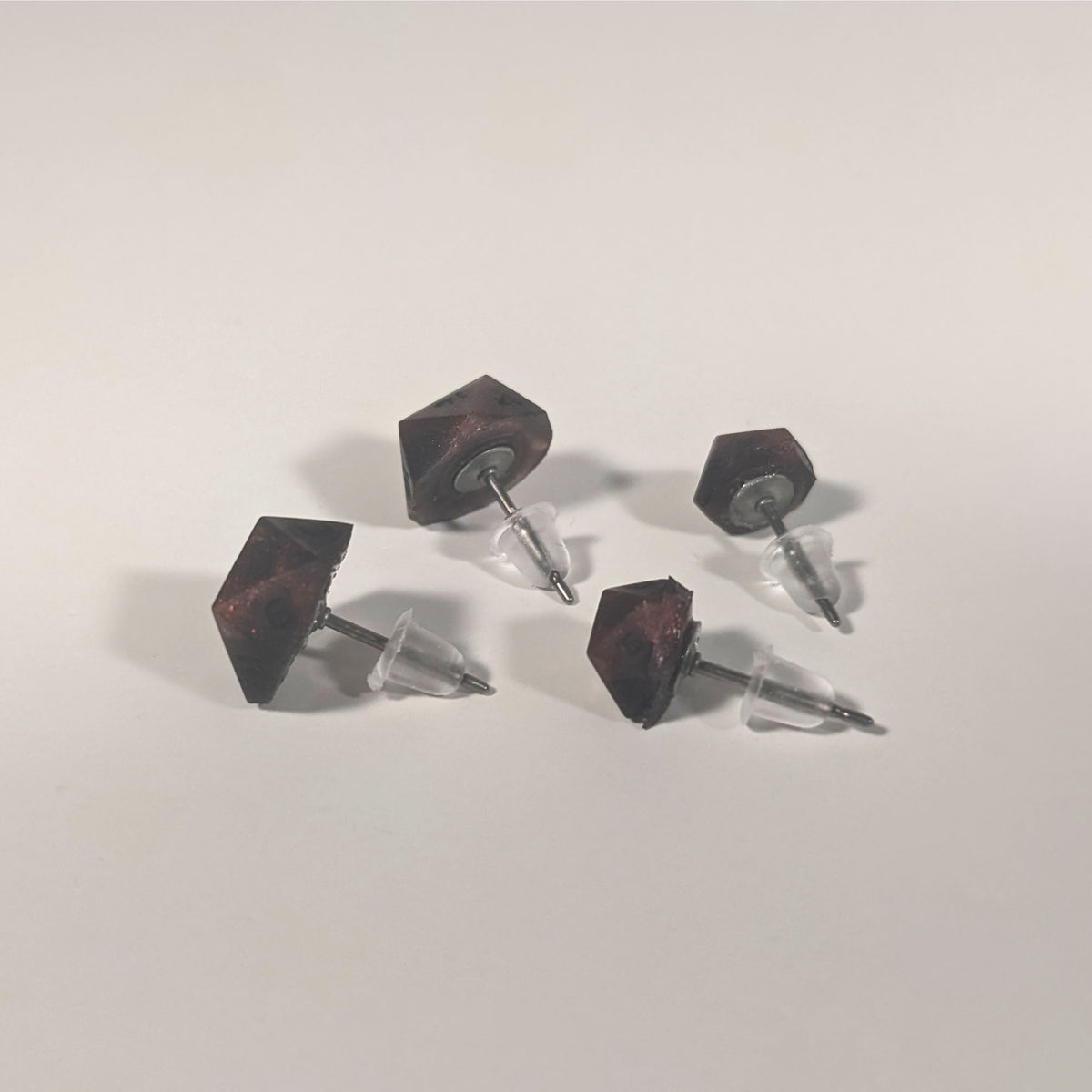 Two pairs of handmade d20 earrings that are swirls of red with black numbers turned to show the titanium hardware and bell shaped rubber backs.