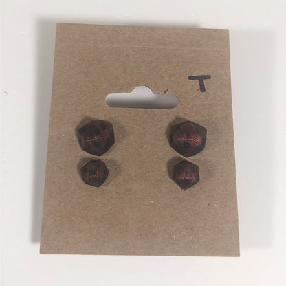Two pairs of handmade d20 earrings with titanium hardware that are swirls of red with black numbers on a kraft brown earring card with a T in the top right corner. The earrings on the left of each pair centers the 20 face and the earrings on the right of each pair centers the 1 face.