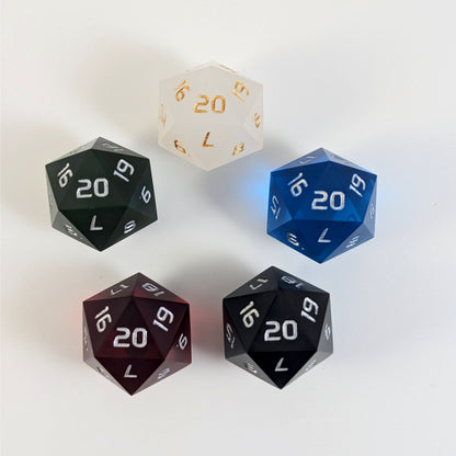 Five spindown d20s with a right spin arranged in a circle with the 20 face on top. White with gold numbers is at the top and blue, black, red, and dark green all with silver numbers follow going clockwise.