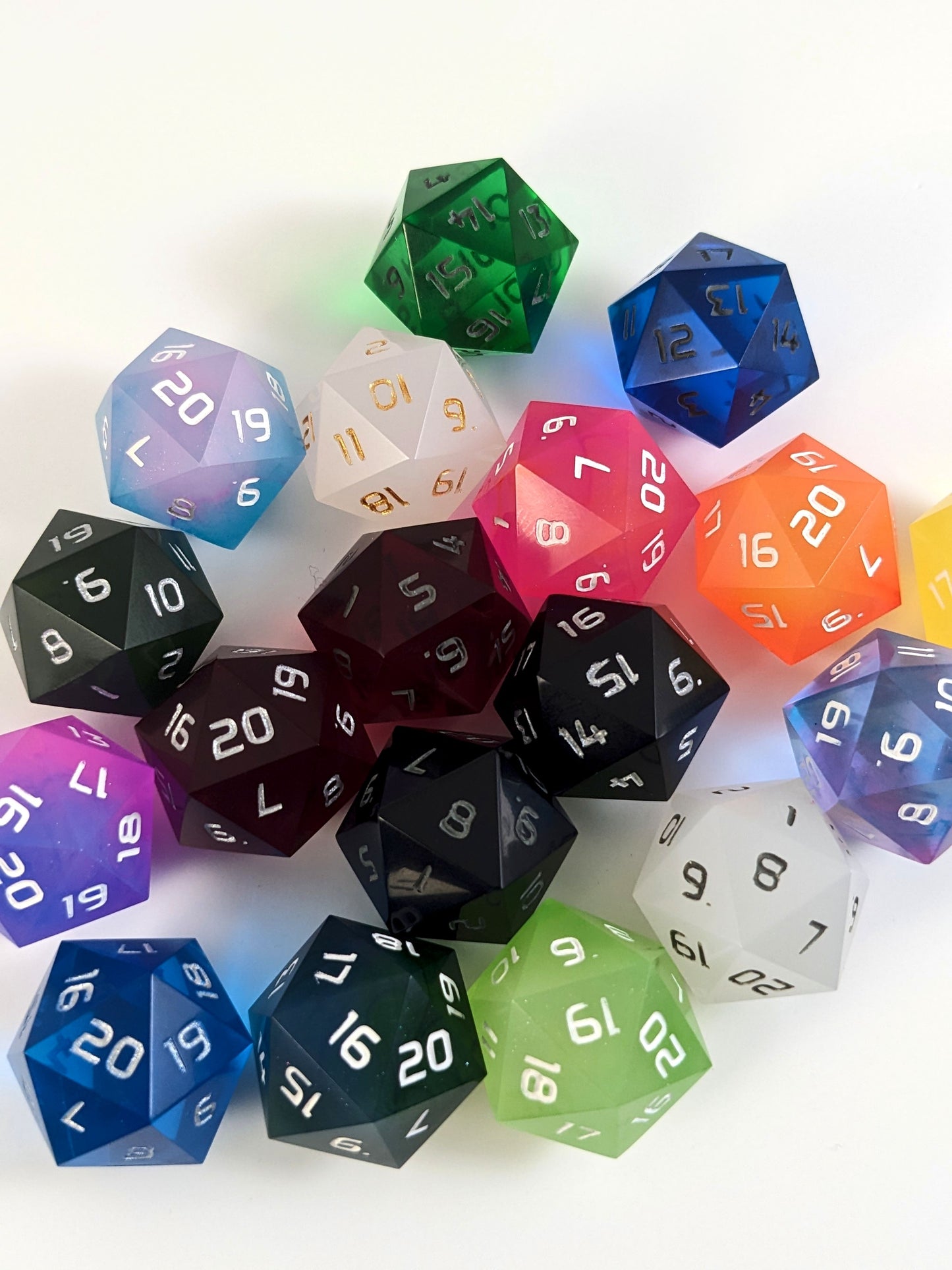 A collection of spindown d20s of a variety of colors on a white background.