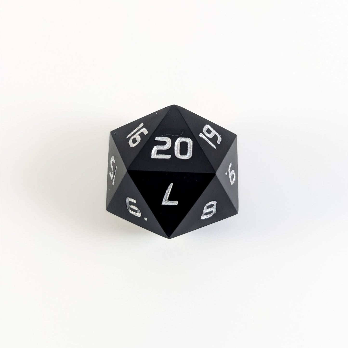 A black spindown d20 with silver numbers and a right spin sits on a white background with the 20 face up.