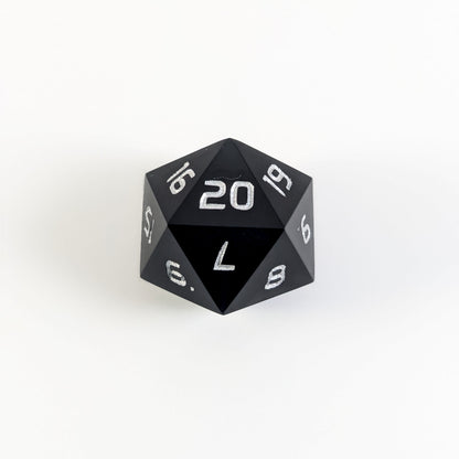 A black spindown d20 with silver numbers and a right spin sits on a white background with the 20 face up.