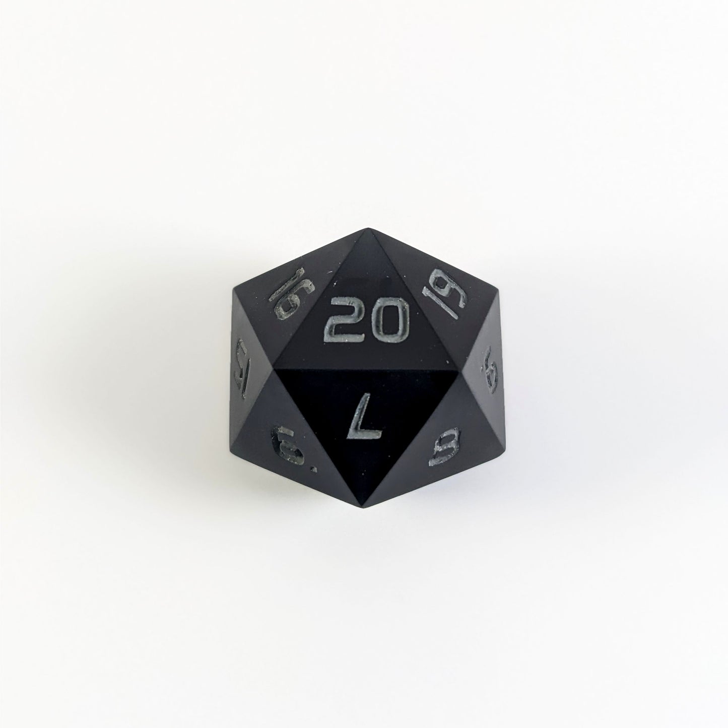 A black spindown d20 with gray numbers and a right spin sits on a white background with the 20 face up.