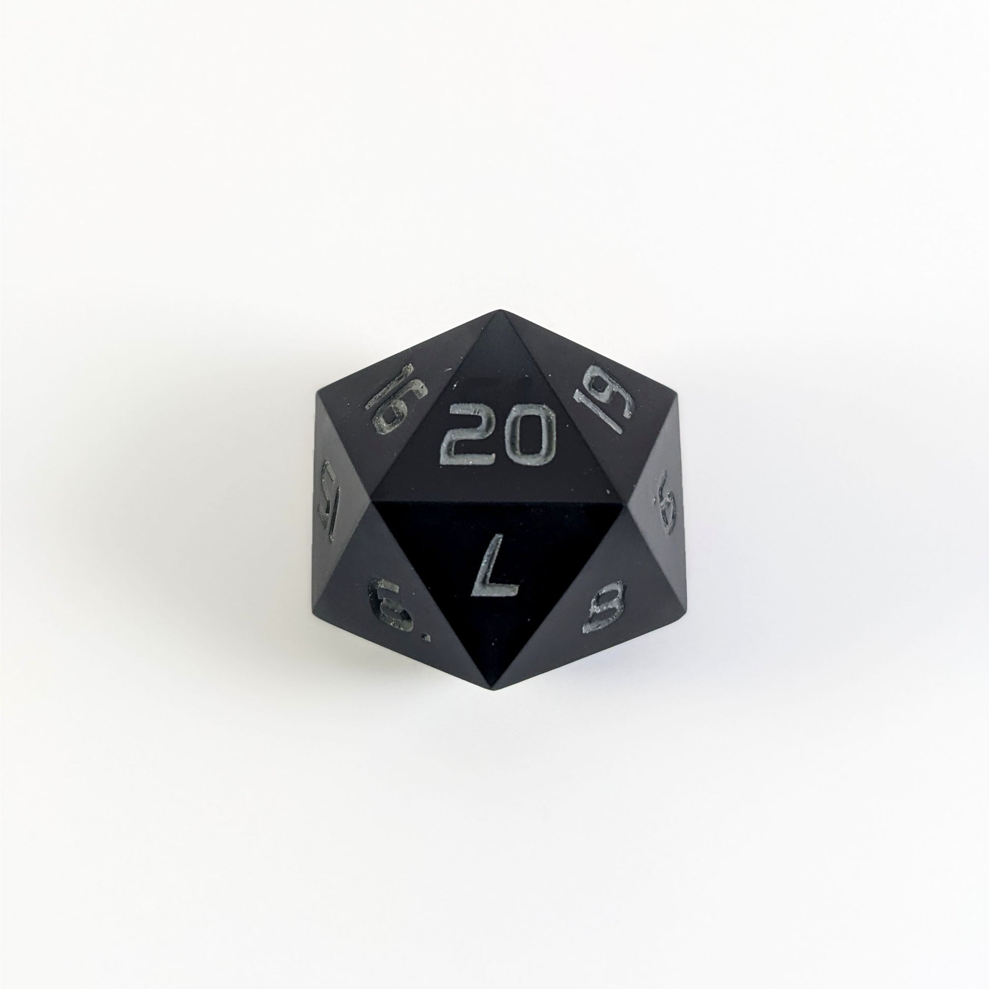 A black spindown d20 with gray numbers and a right spin sits on a white background with the 20 face up.