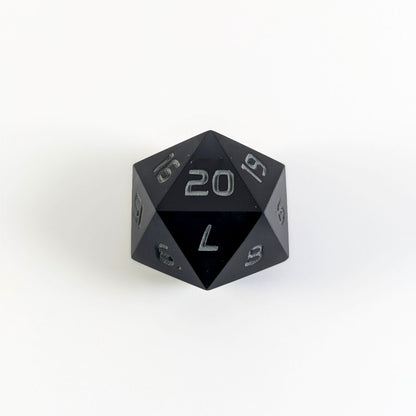 A black spindown d20 with gray numbers and a right spin sits on a white background with the 20 face up.