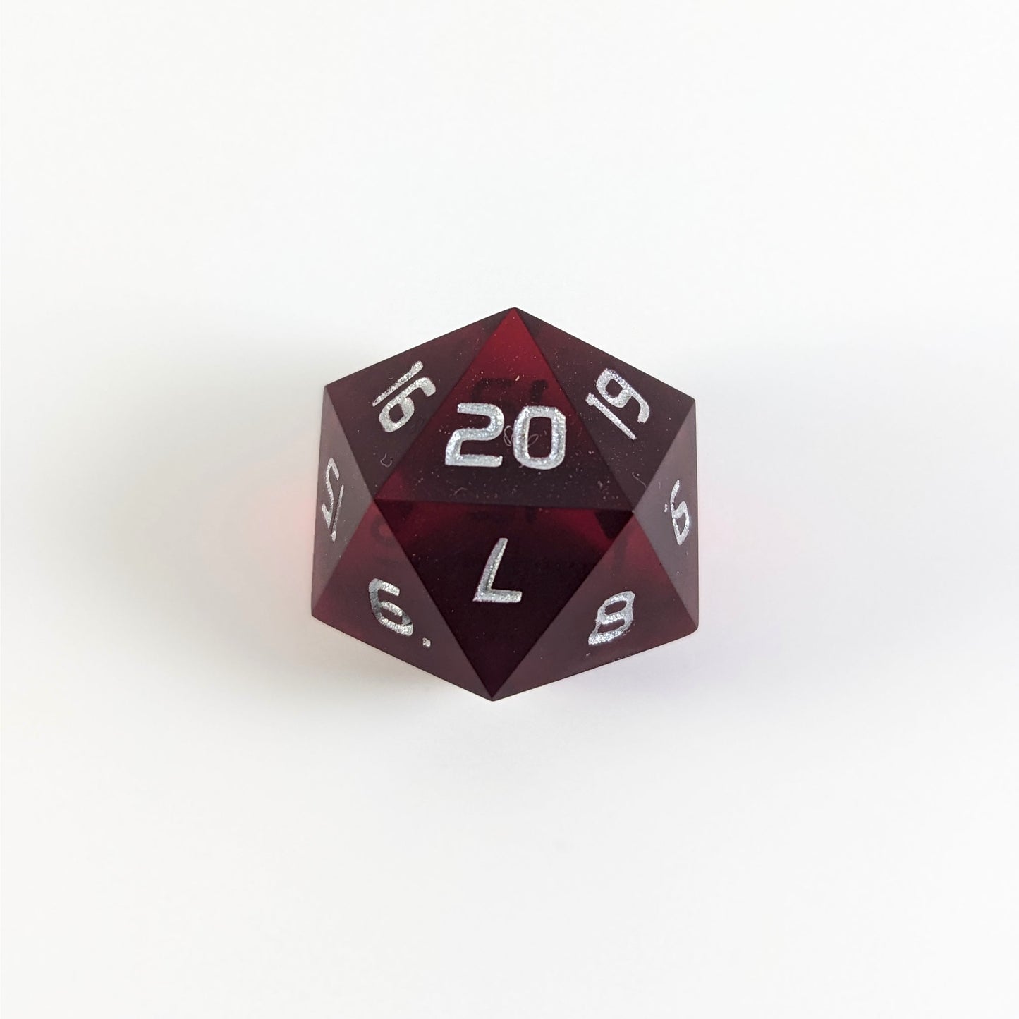 A red spindown d20 with silver numbers and a right spin sits on a white background with the 20 face up.