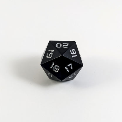 A low angle of a black spindown d20 with silver numbers and a right spin sits on a white background with the 20 through 16 corner facing the camera showing the spiral of the spin down.