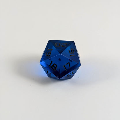 A low angle of a blue spindown d20 with gray numbers and a right spin sits on a white background with the 20 through 16 corner facing the camera showing the spiral of the spin down.