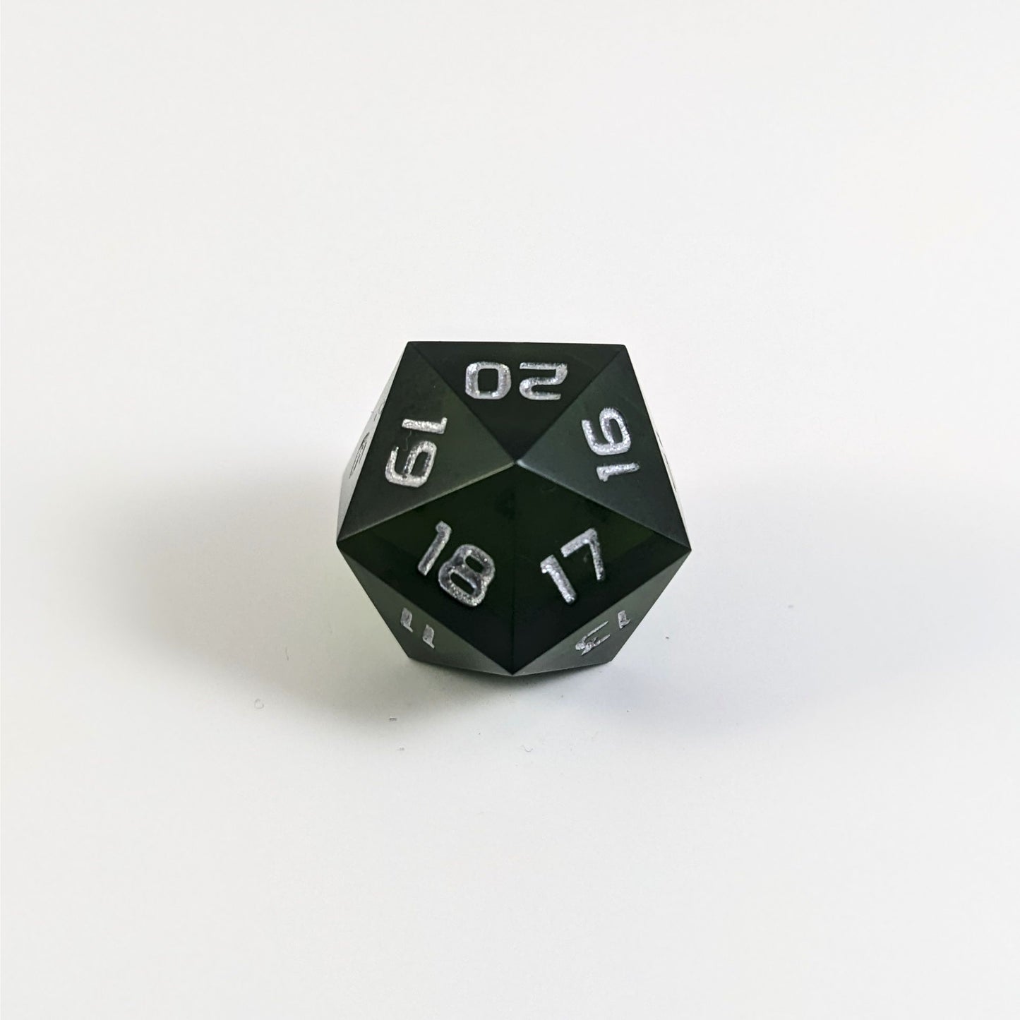 A low angle of a dark green spindown d20 with silver numbers and a right spin sits on a white background with the 20 through 16 corner facing the camera showing the spiral of the spin down.