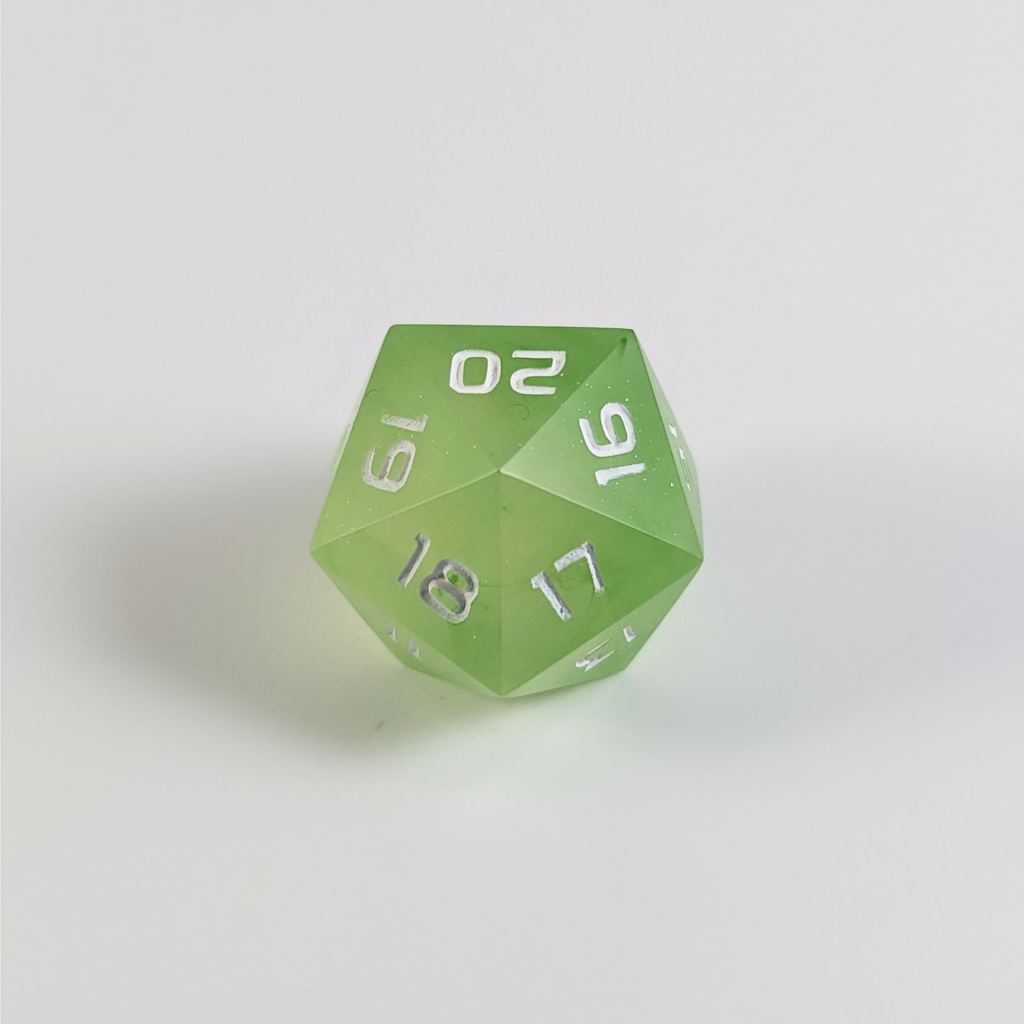 A low angle of a yellow green spindown d20 with white numbers and a right spin sits on a white background with the 20 through 16 corner facing the camera showing the spiral of the spin down.