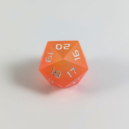 A low angle of an orange spindown d20 with white numbers and a right spin sits on a white background with the 20 through 16 corner facing the camera showing the spiral of the spin down.