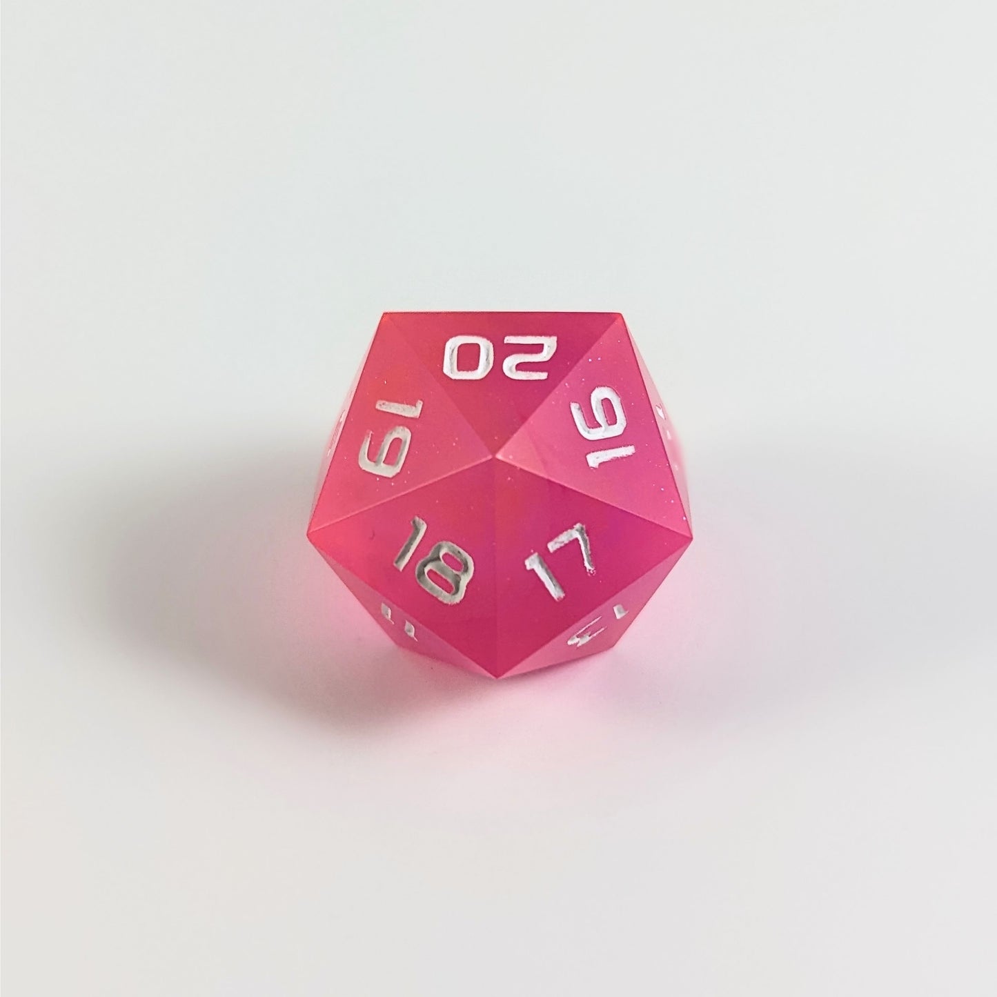 A low angle of a magenta spindown d20 with white numbers and a right spin sits on a white background with the 20 through 16 corner facing the camera showing the spiral of the spin down.