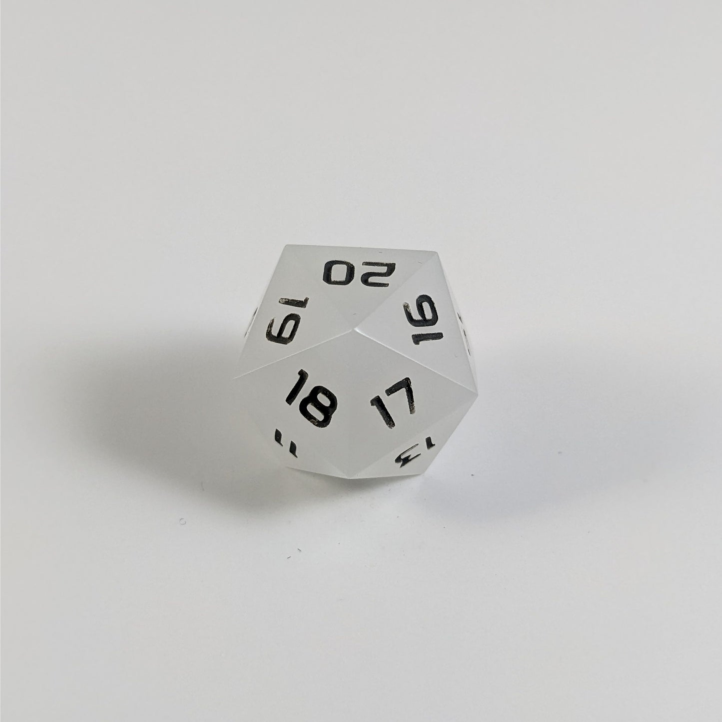 A low angle of a white spindown d20 with gray numbers and a right spin sits on a white background with the 20 through 16 corner facing the camera showing the spiral of the spin down.
