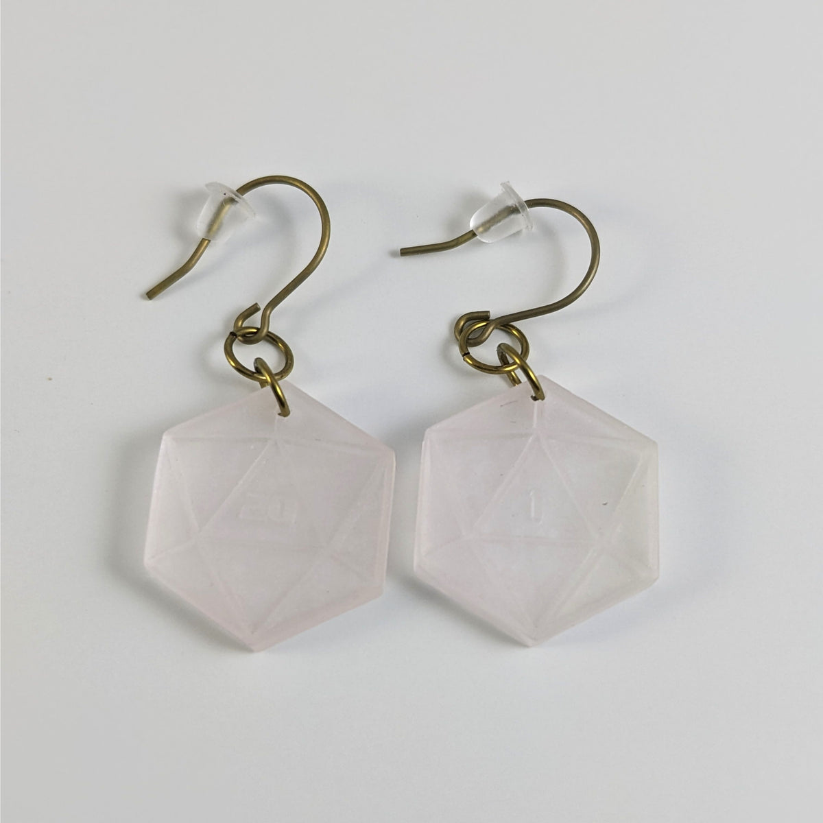 A pair of pale pink and white dangly, flat d20 earrings with gold color titanium and niobium hardware and bell shaped rubber backs on a white background. The earring on the left has a 20 on it and the earring on the right has a 1 on it, both in a sci-fi style font.