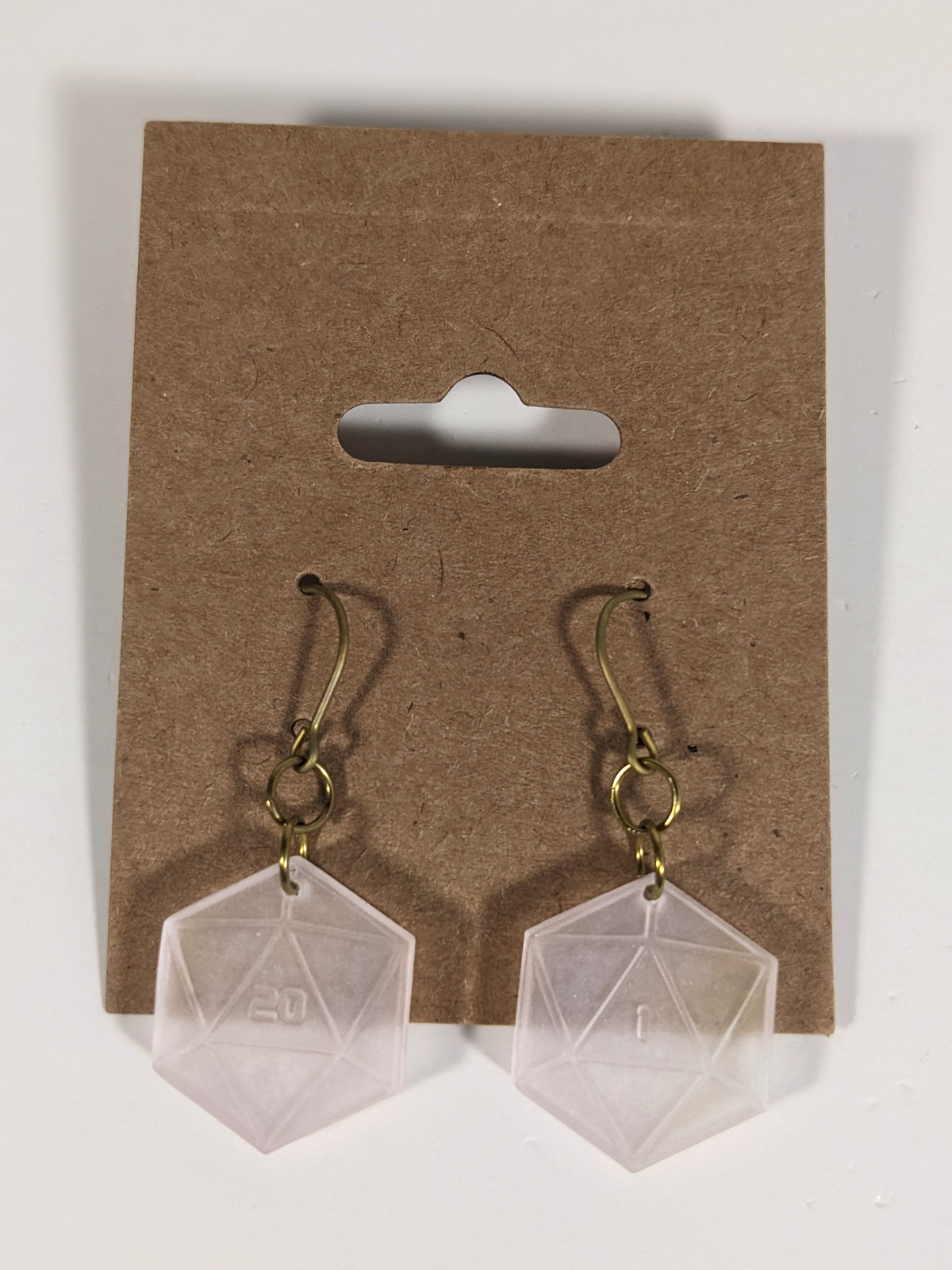 A pair of pale pink and white dangly, flat d20 earrings with gold color titanium and niobium hardware on a kraft earring card on a white background. The earring on the left has a 20 on it and the earring on the right has a 1 on it, both in a sci-fi style font.