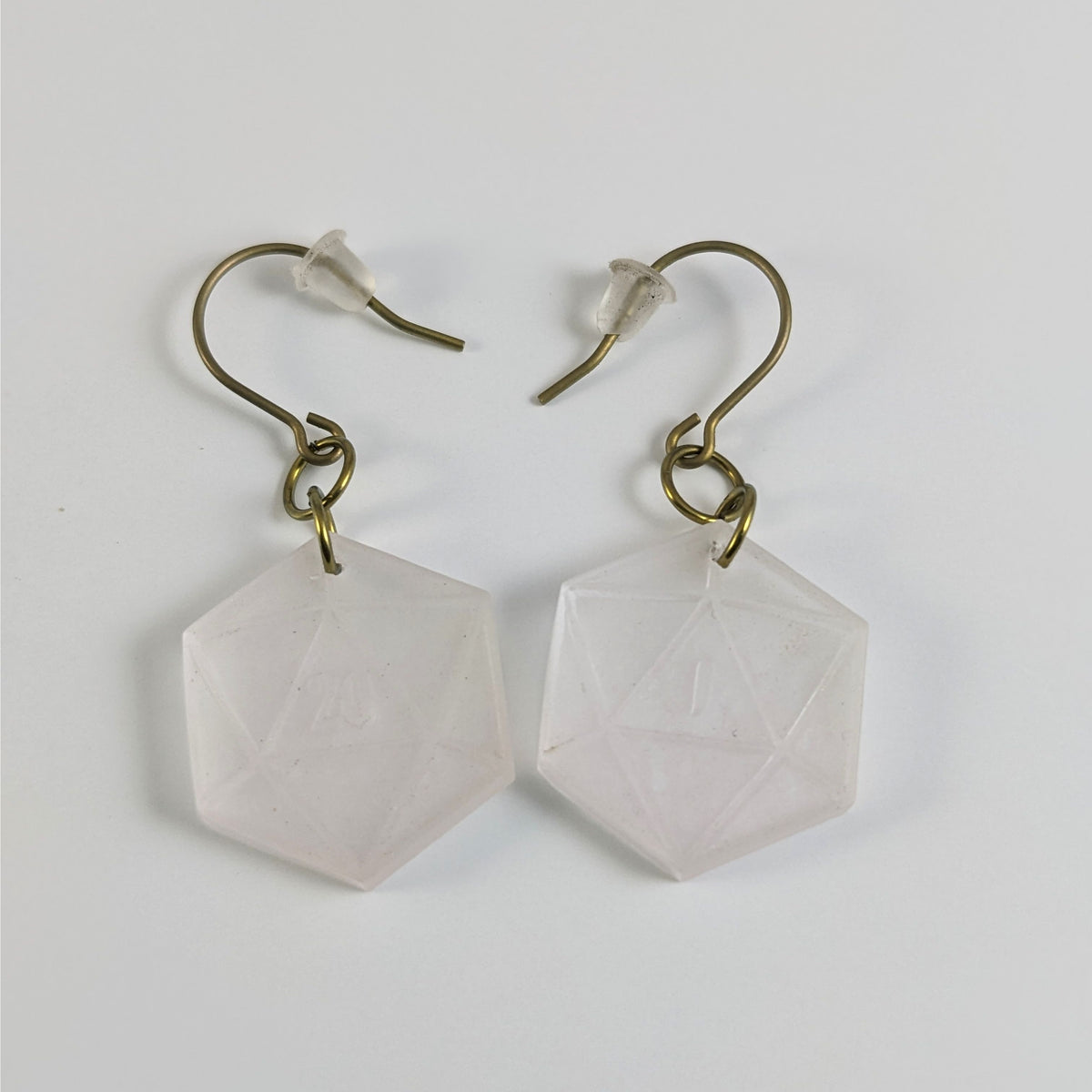 A pair of pale pink and white dangly, flat d20 earrings with gold color titanium and niobium hardware and bell shaped rubber backs on a white background. The earring on the left has a 20 on it and the earring on the right has a 1 on it, both in a fantasy style font.