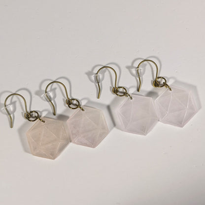 Two pairs of pale pink and white dangly, flat d20 earrings with gold color titanium and niobium hardware and bell shaped rubber backs on a white background.