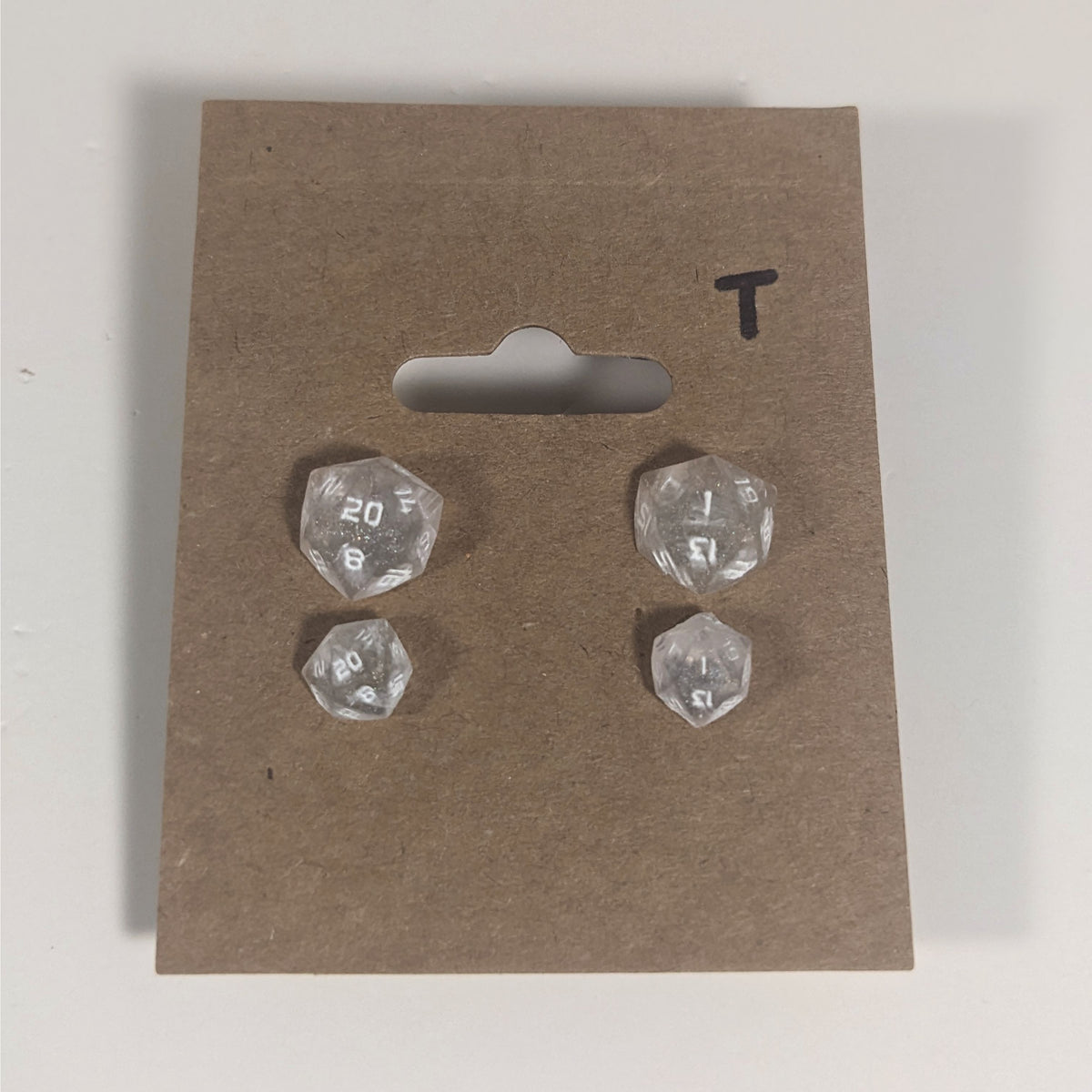 Two pairs of handmade d20 earrings with titanium hardware that are faded pink and translucent white with white numbers on a kraft brown earring card with a T in the top right corner. The earrings on the left of each pair centers the 20 face and the earrings on the right of each pair centers the 1 face.