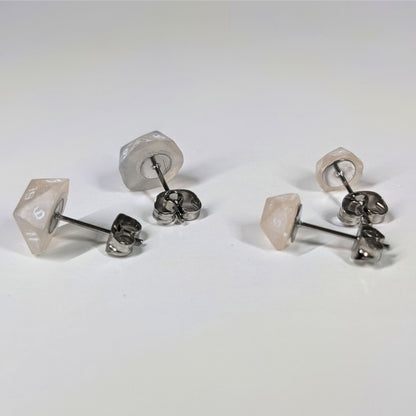Two pairs of handmade d20 earrings that are light pink and white with white numbers turned to show the metal alloy hardware and butterfly backs.