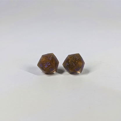 A single pair of the larger size handmade d20 earrings with sterling silver hardware that are dark gold with purple numbers on a white background. The earring on the left centers the 20 face and the earring on the right centers the 1 face.
