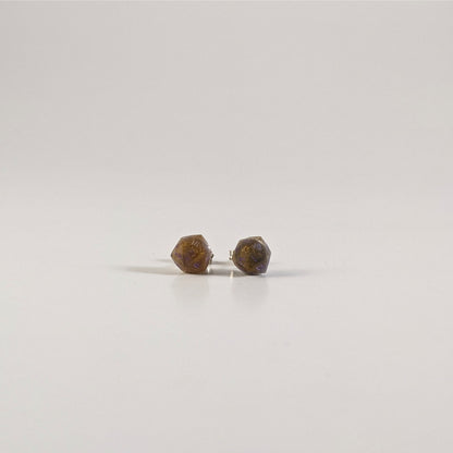 A single pair of the smaller size handmade d20 earrings with sterling silver hardware that are dark gold with purple numbers on a white background. The earring on the left centers the 20 face and the earring on the right centers the 1 face.