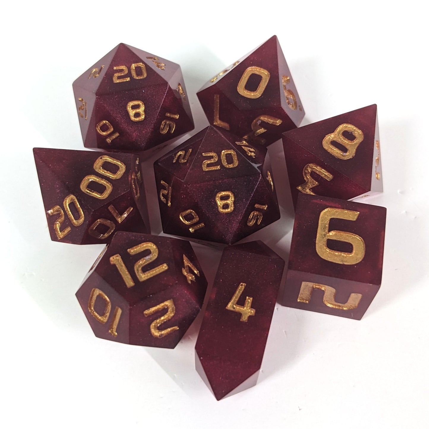 A complete set of 8 handmade artisan dice that are bold red with gold numbers. The DnD dice set is arranged in a circle and features 2 D20s, one of which is in the center surrounded by the other 7 dice on a white background. The d4 is a unique, crystalline shape.