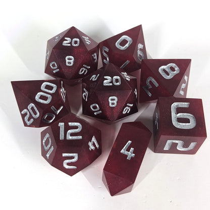 A complete set of 8 handmade artisan dice that are bold red with silver numbers. The DnD dice set is arranged in a circle and features 2 D20s, one of which is in the center surrounded by the other 7 dice on a white background. The d4 is a unique, crystalline shape.