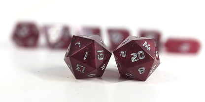 A straight on photo of a standard set of DnD dice that are bold red with silver numbers focusing on 2 d20s in the center. The d20 on the left has the 1 face centered and the d20 on the right has the 20 face centered. The other 6 dice are lined up in the background but are out of focus, while the d20s are in sharp focus.