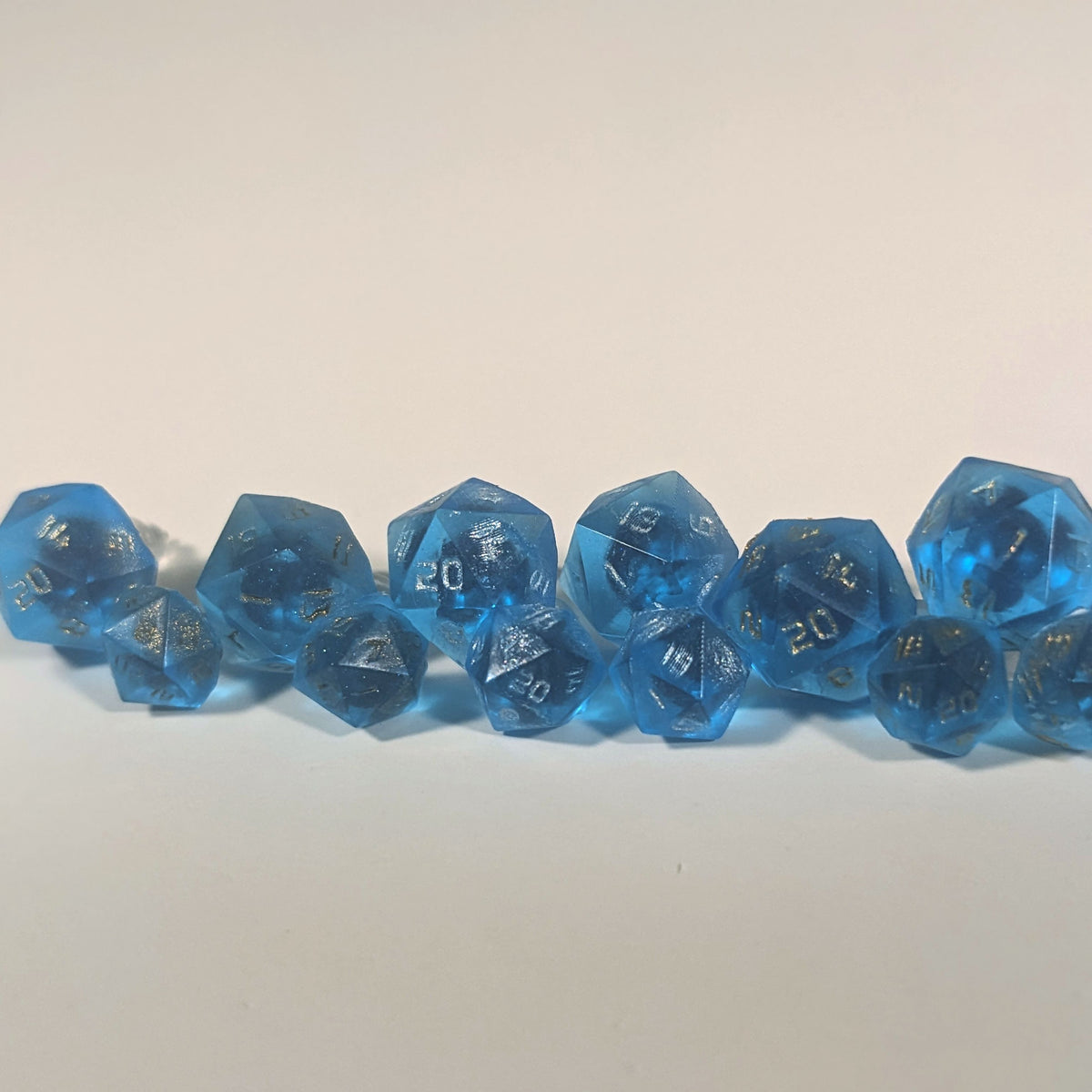 Six pairs of sapphire blue d20 stud earrings with titanium hardware on a white background. There are 3 large pairs and 3 small pairs, and one pair of each of those has gold numbers, silver numbers, and bronze numbers.