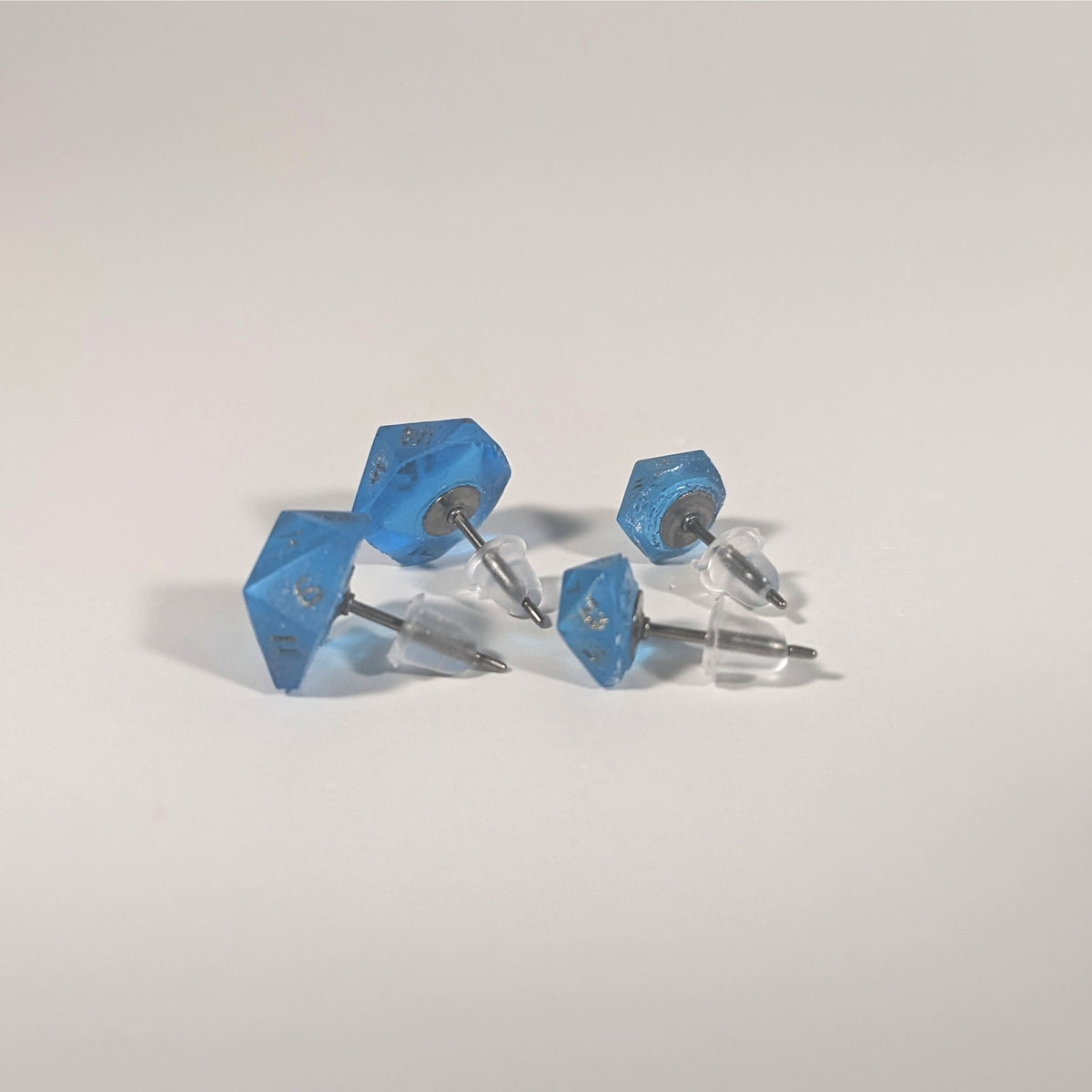 Two pairs of handmade d20 earrings that are sapphire blue with bronze numbers turned to show the titanium hardware and bell shaped rubber backs.