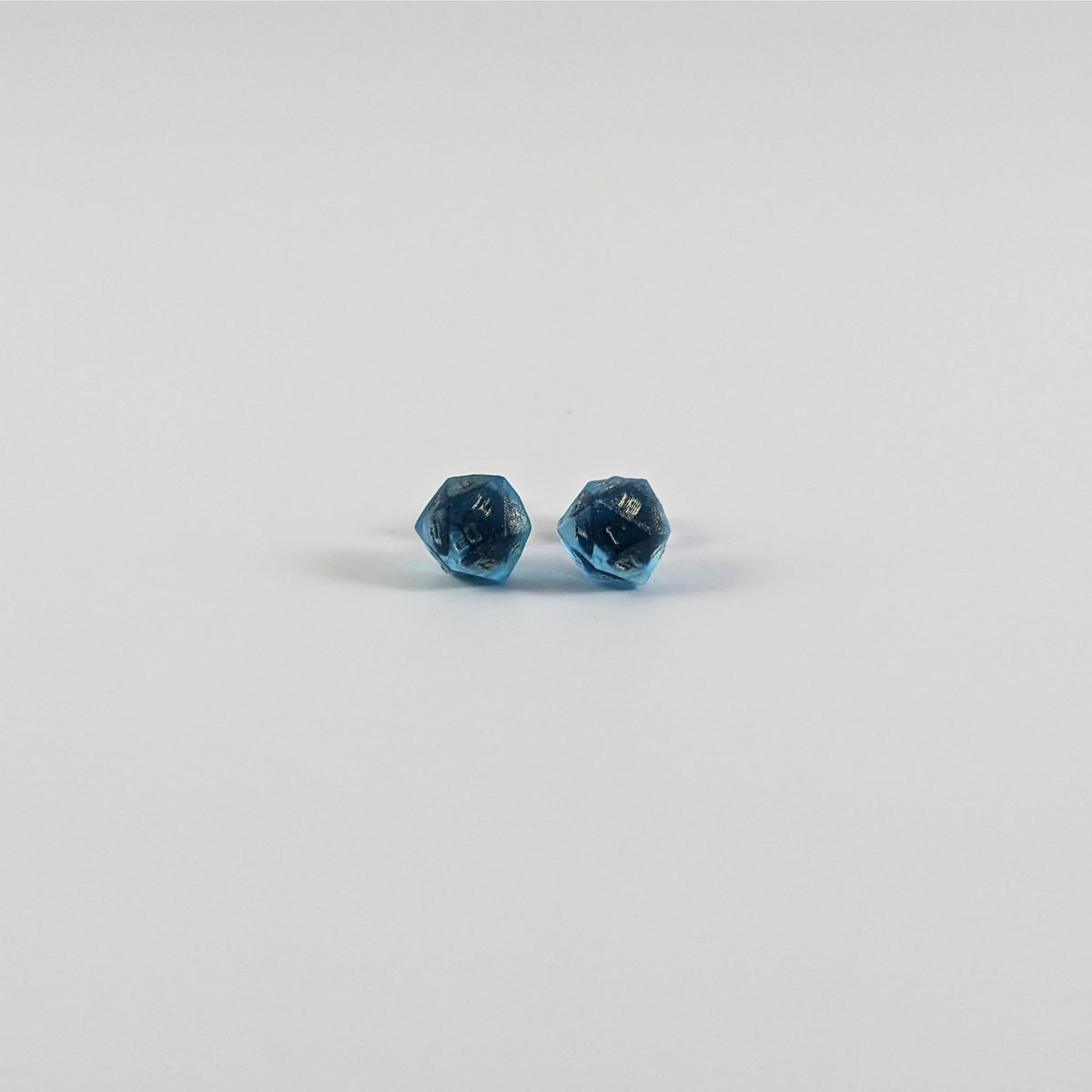 A single pair of the smaller size handmade d20 earrings with titanium hardware that are sapphire blue with bronze numbers on a white background. The earring on the left centers the 20 face and the earring on the right centers the 1 face.