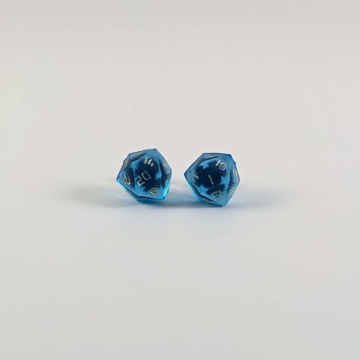 A single pair of the larger size handmade d20 earrings with titanium hardware that are sapphire blue with gold numbers on a white background. The earring on the left centers the 20 face and the earring on the right centers the 1 face.
