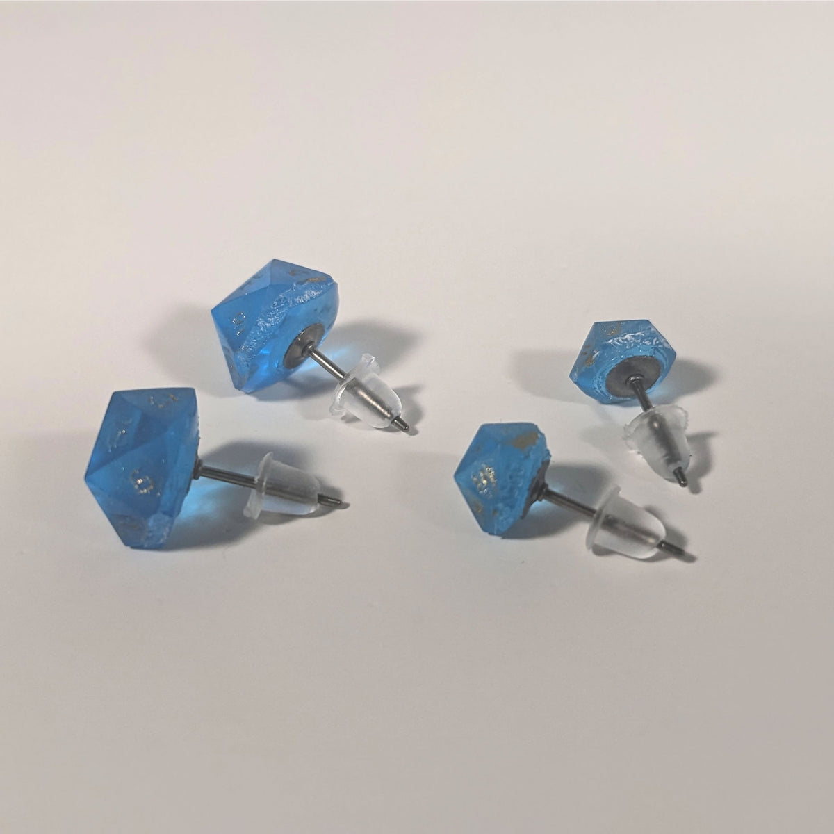 Two pairs of handmade d20 earrings that are sapphire blue with gold numbers turned to show the titanium hardware and bell shaped rubber backs.