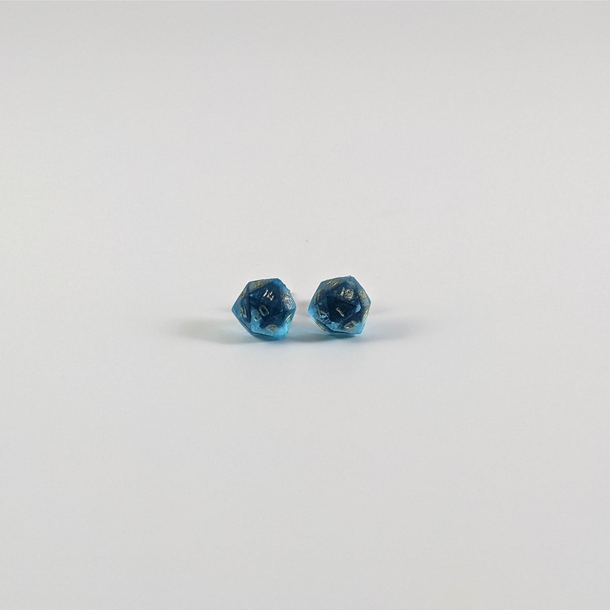 A single pair of the smaller size handmade d20 earrings with titanium hardware that are sapphire blue with gold numbers on a white background. The earring on the left centers the 20 face and the earring on the right centers the 1 face.