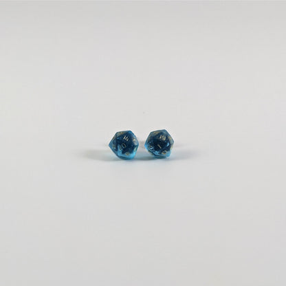 A single pair of the smaller size handmade d20 earrings with titanium hardware that are sapphire blue with gold numbers on a white background. The earring on the left centers the 20 face and the earring on the right centers the 1 face.