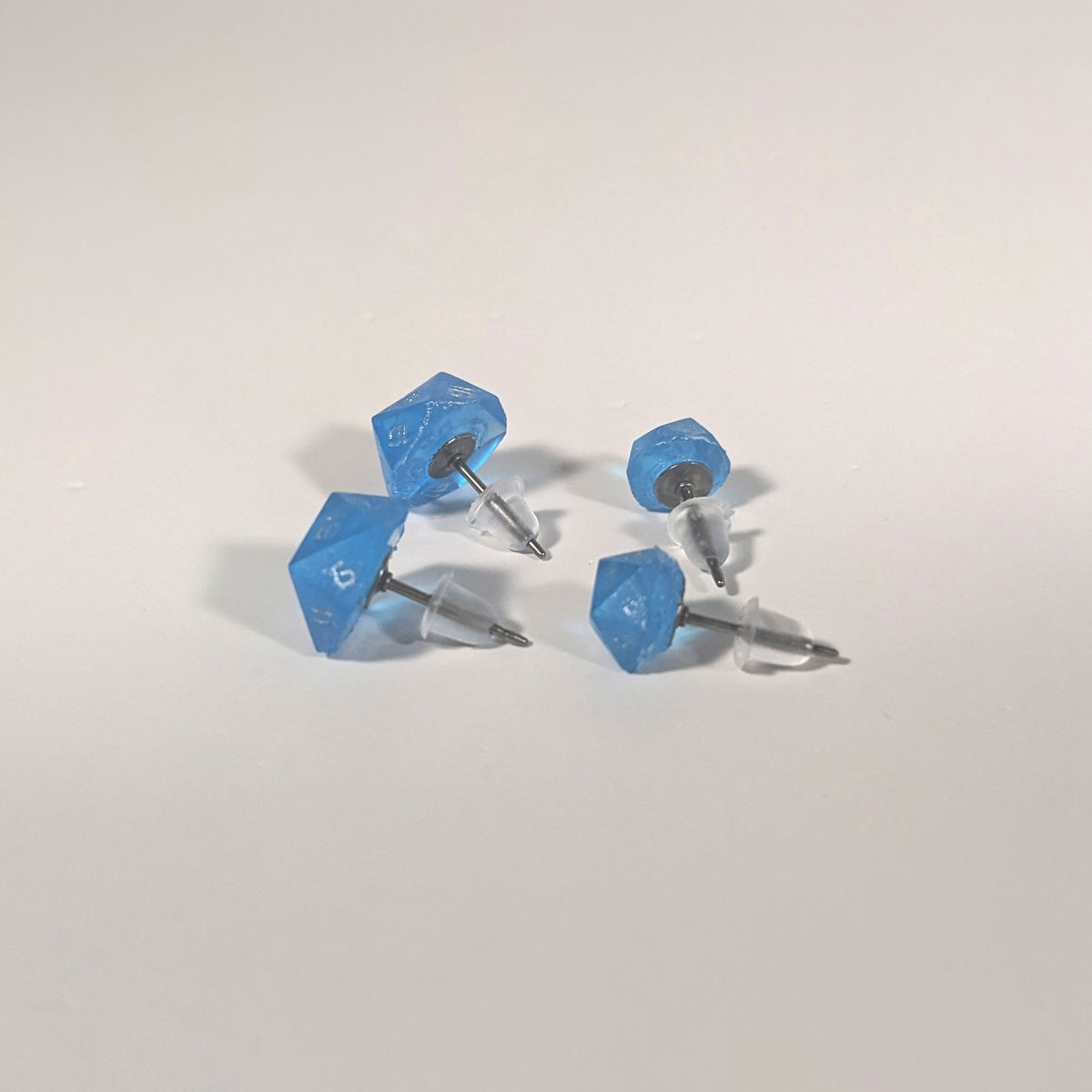 Two pairs of handmade d20 earrings that are sapphire blue with silver numbers turned to show the titanium hardware and bell shaped rubber backs.