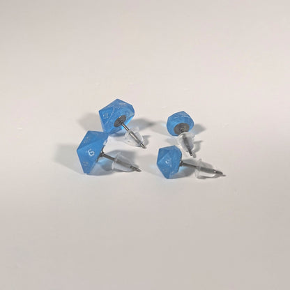 Two pairs of handmade d20 earrings that are sapphire blue with silver numbers turned to show the titanium hardware and bell shaped rubber backs.