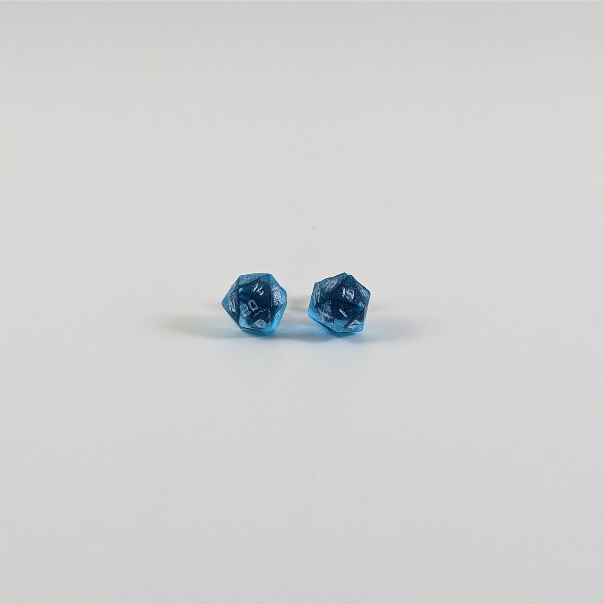 A single pair of the smaller size handmade d20 earrings with titanium hardware that are sapphire blue with silver numbers on a white background. The earring on the left centers the 20 face and the earring on the right centers the 1 face.