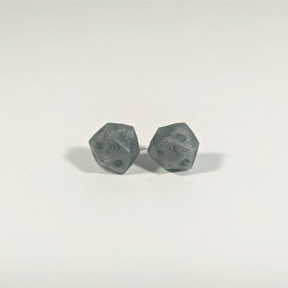 A single pair of the larger size handmade d20 earrings with titanium hardware that are dark silver with forest green numbers on a white background. The earring on the left centers the 20 face and the earring on the right centers the 1 face.