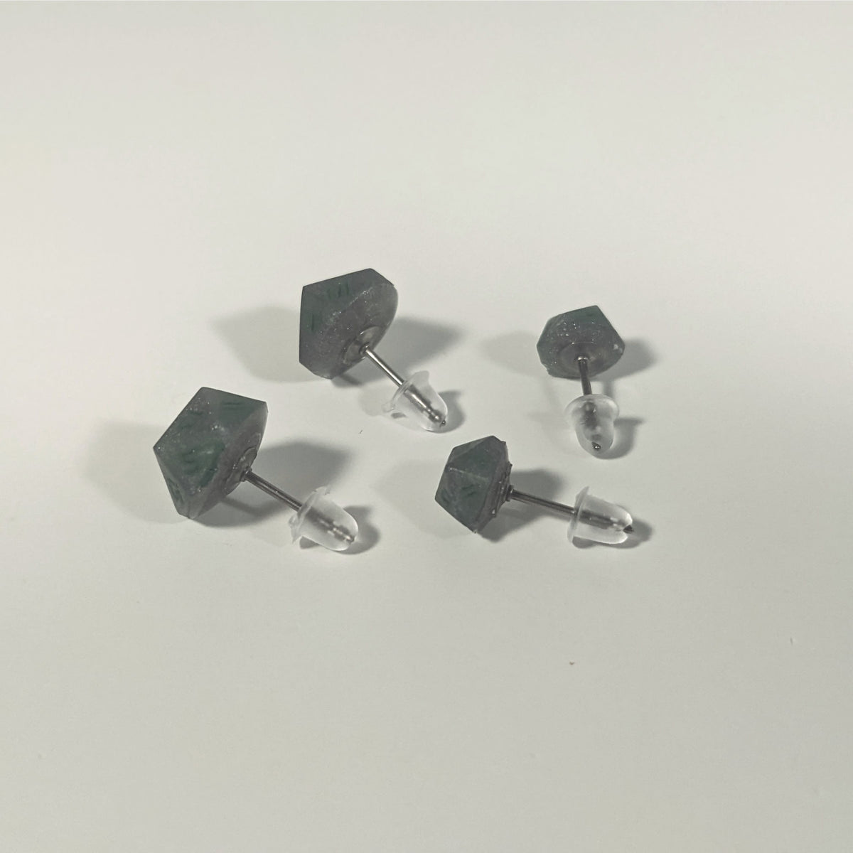 Two pairs of handmade d20 earrings that are dark silver with forest green numbers turned to show the titanium hardware and bell shaped rubber backs.