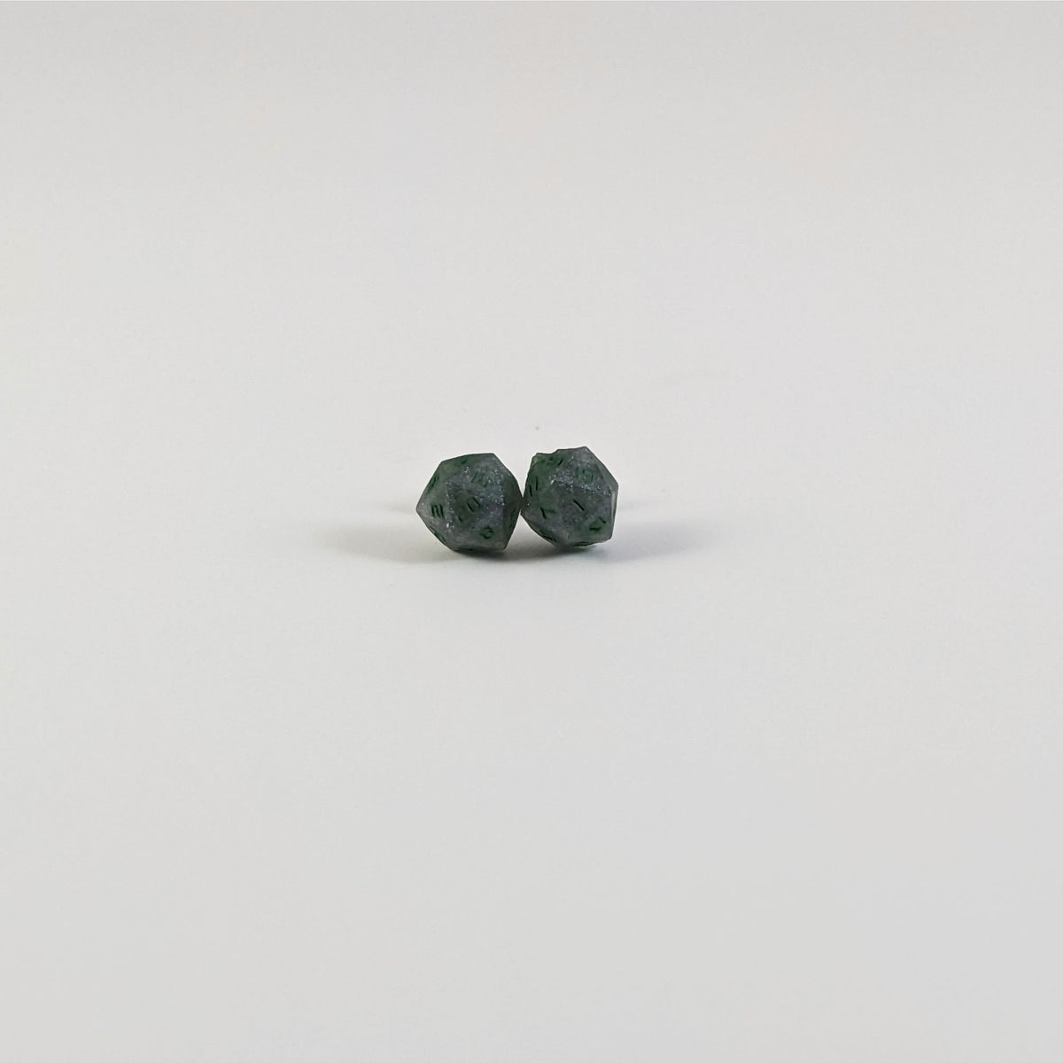 A single pair of the smaller size handmade d20 earrings with titanium hardware that are dark silver with forest green numbers on a white background. The earring on the left centers the 20 face and the earring on the right centers the 1 face.