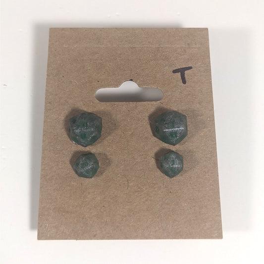 Two pairs of handmade d20 earrings with titanium hardware that are dark silver with forest green numbers on a kraft brown earring card with a T in the top right corner. The earrings on the left of each pair centers the 20 face and the earrings on the right of each pair centers the 1 face.