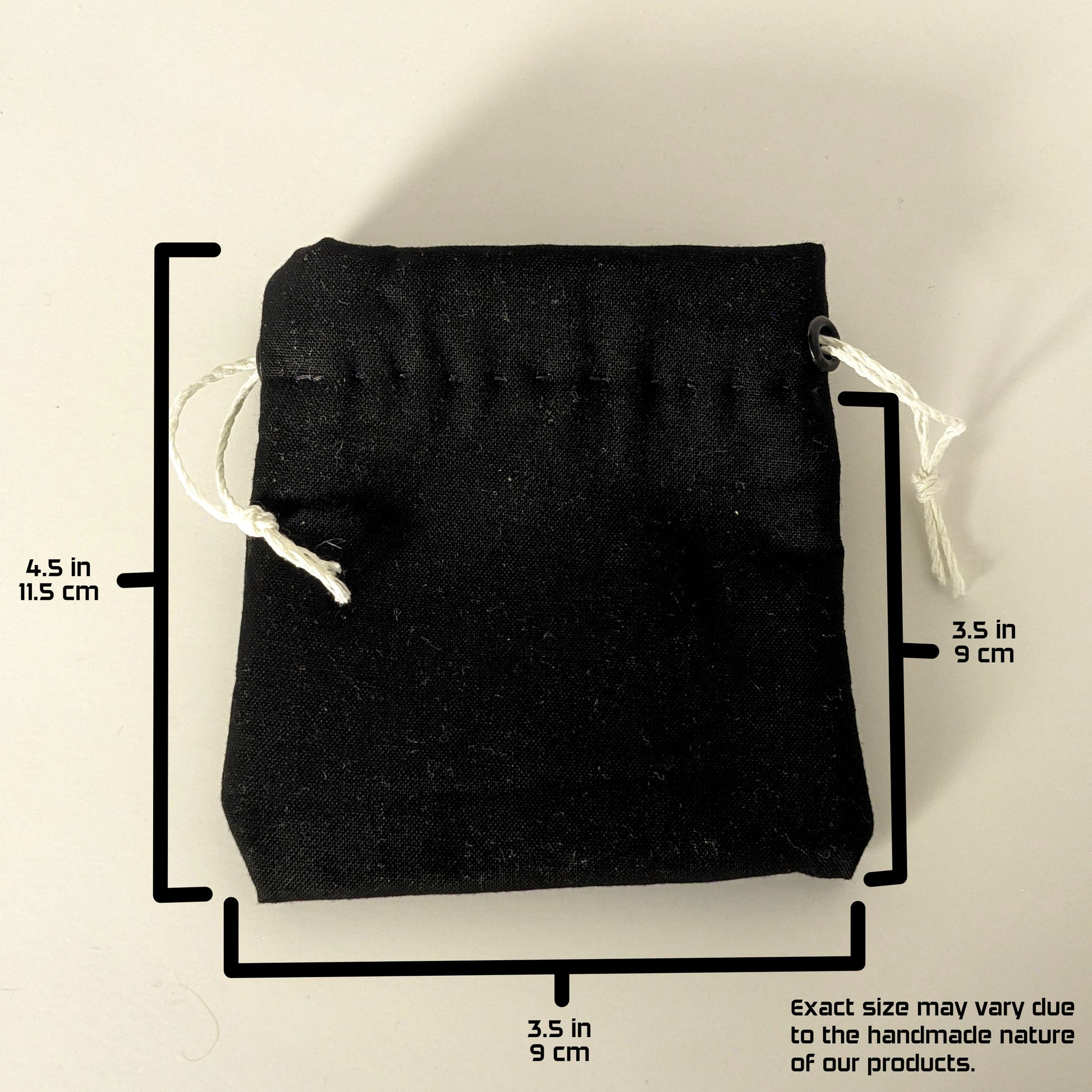 A handmade, black, small size dice bag with white drawstrings lays flat on a white background. The graphic includes overlays showing the full height of the dice bag as 4.5 inches or 11.5 cm, the width of the dice bag as 3.5 inches or 9 cm, and the height from bottom to drawstring as 3.5 inches or 9 cm. A note in the bottom right corner states "Exact size my vary due to the handmade nature of our products."